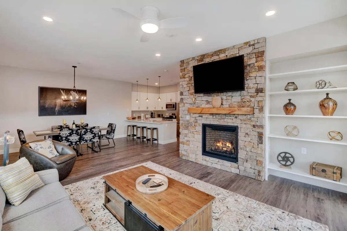 The image showcases a spacious and inviting living area with a glowing fireplace as the centerpiece, a cozy sofa perfect for unwinding, elegant artwork on the walls, and a dining table set for shared meals. The setting exudes warmth and comfort, ideal for family and friends to gather, relax, and create lasting memories.