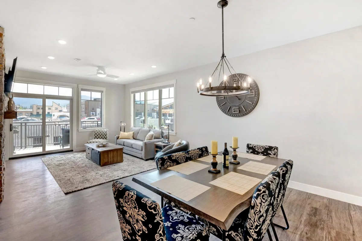 A spacious, open-plan area that seamlessly blends a stylish dining table, comfortable sofa, chandelier, and large windows. The room is filled with natural light and designed for both family meals and relaxing while enjoying the view or watching TV.