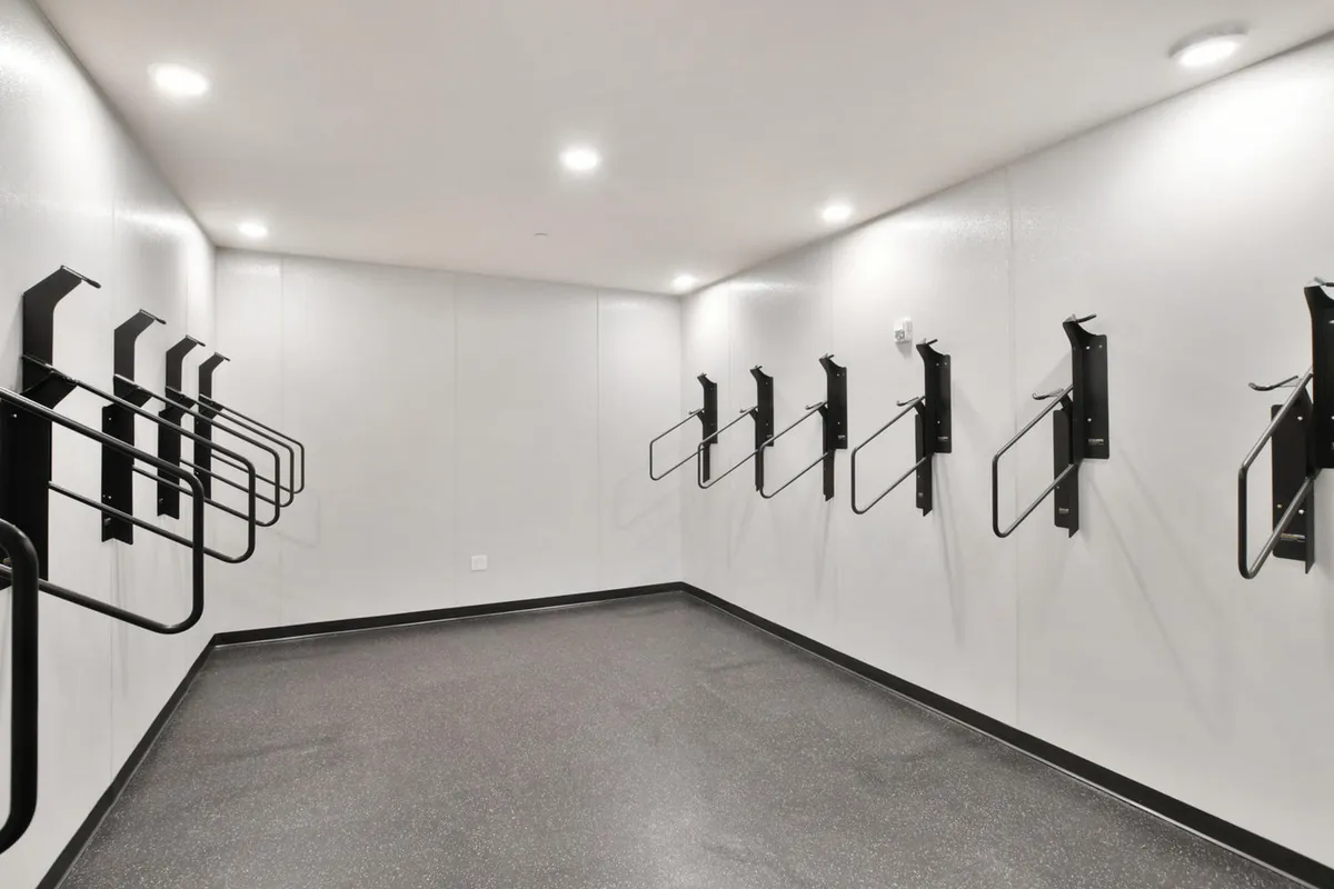 This image showcases a clean and well-organized indoor bike storage area featuring black bike racks mounted along smooth white walls and a dark floor. The space is designed for easy access and secure storage, reflecting functionality and a sense of community among cyclists.
