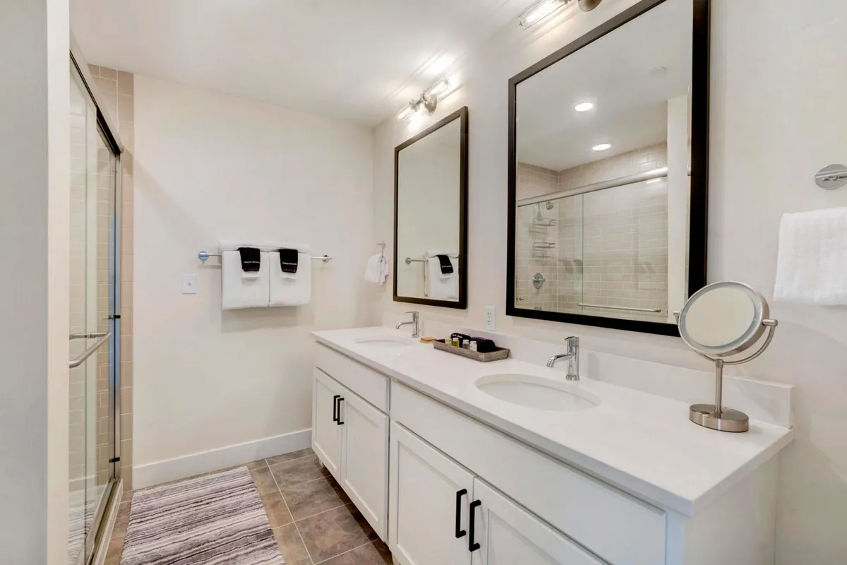 A modern, spa-inspired bathroom boasting a double vanity with two sinks, large mirrors, and a spacious shower area. The clean design and ample amenities evoke a calming, luxurious vibe.