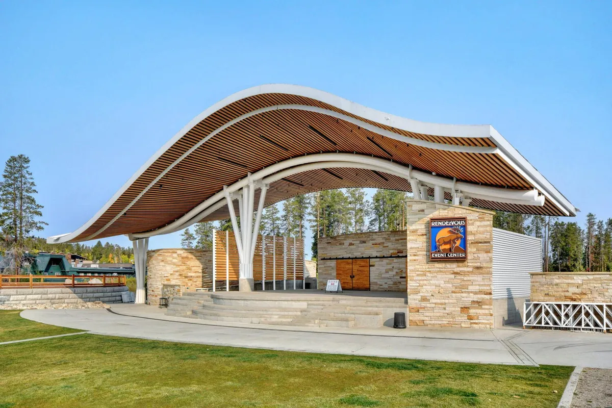 This image features the distinctive curved roof and stone facade of the Hideaway Park Amphitheater, with clear event center signage visible. The setting is outdoors, suggesting an active hub for concerts, festivals, and community events, with an atmosphere of celebration and gathering.