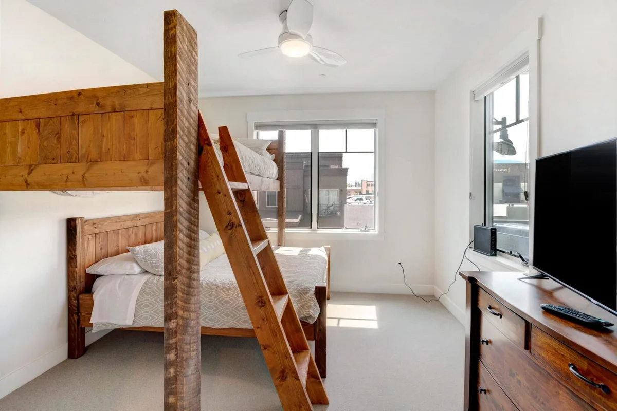 A cozy kids’ or group bedroom with a full-over-queen bunk bed, a window streaming in natural light, and a TV unit. The playful yet relaxed atmosphere suits families or groups seeking a welcoming retreat for children or extra guests.